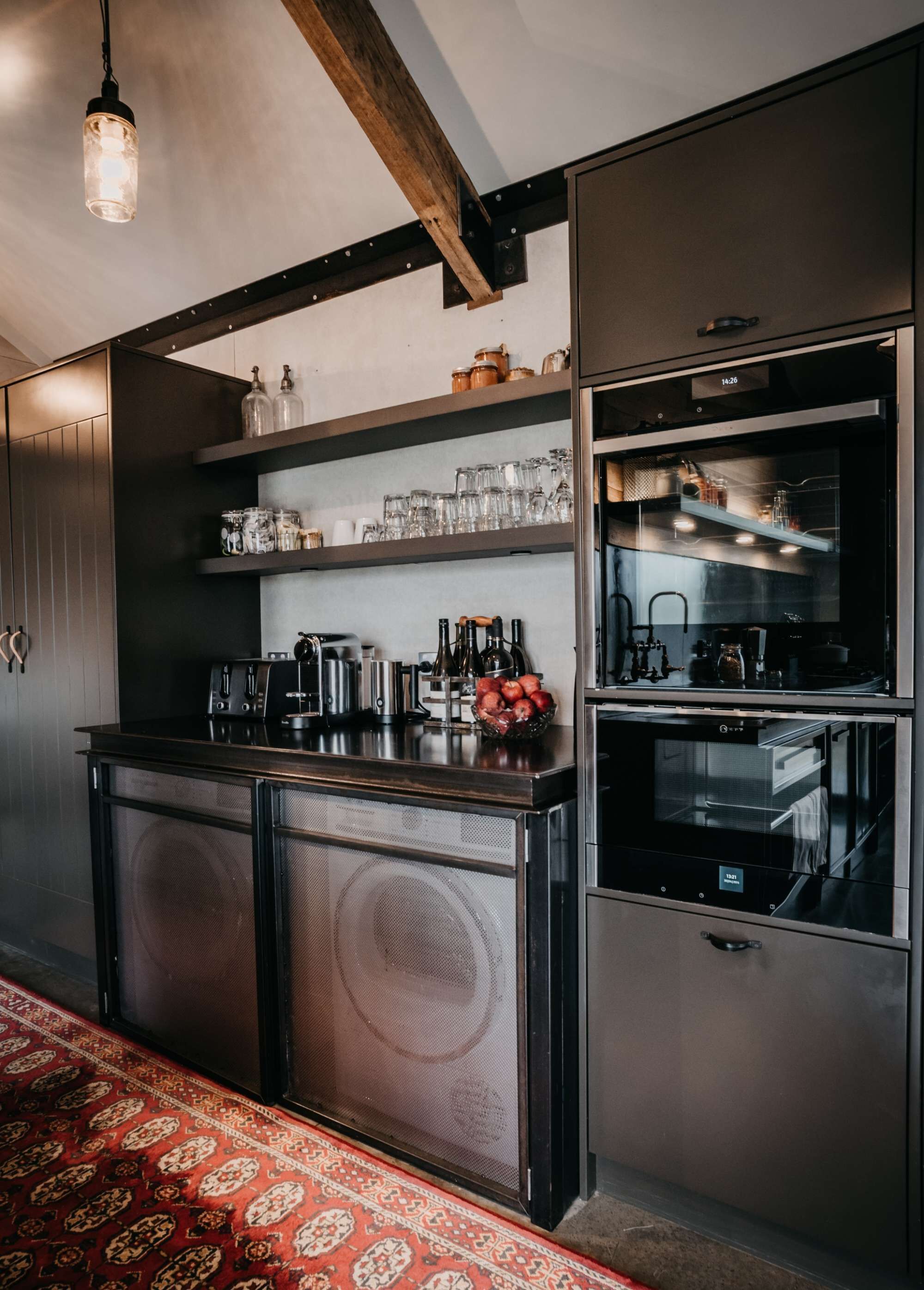 Una cucina moderna con elettrodomestici in acciaio inossidabile, travi in legno e un tappeto rosso con motivi.