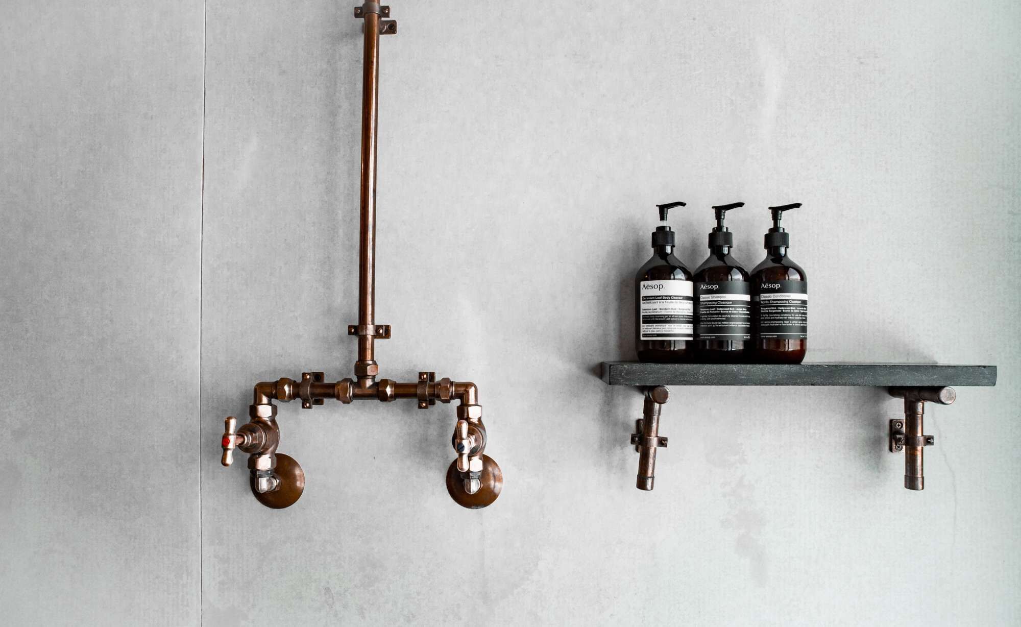 A bathroom with a copper faucet, a showerhead, and three bottles of Aesop shampoo and conditioner on a shelf.