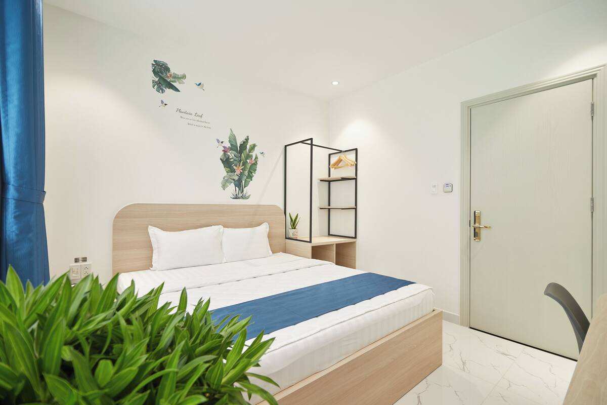 Ein ordentlich eingerichtetes Schlafzimmer mit einem Bett, einer Zimmerpflanze, einem Wandregal und einer Tür.