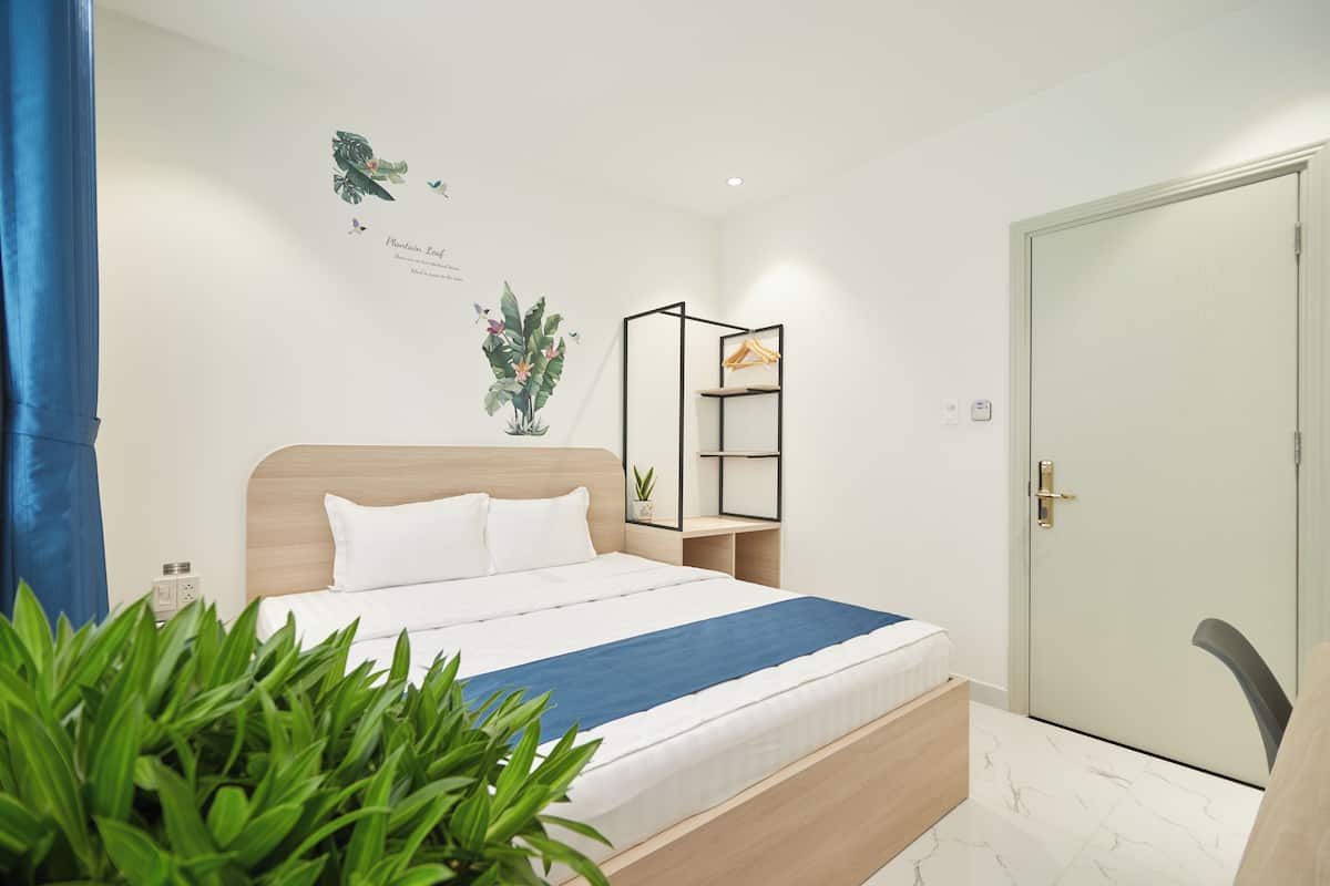 A neatly arranged bedroom with a bed, a bedside plant, a wall-mounted shelf, and a door.