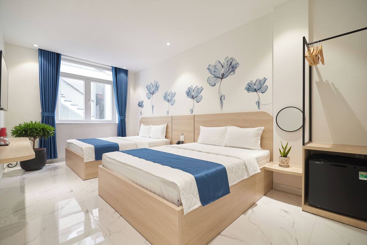 Ein Hotelzimmer mit zwei Betten, einem Schreibtisch, einem Kühlschrank und einer Wand mit floralen Bildern.