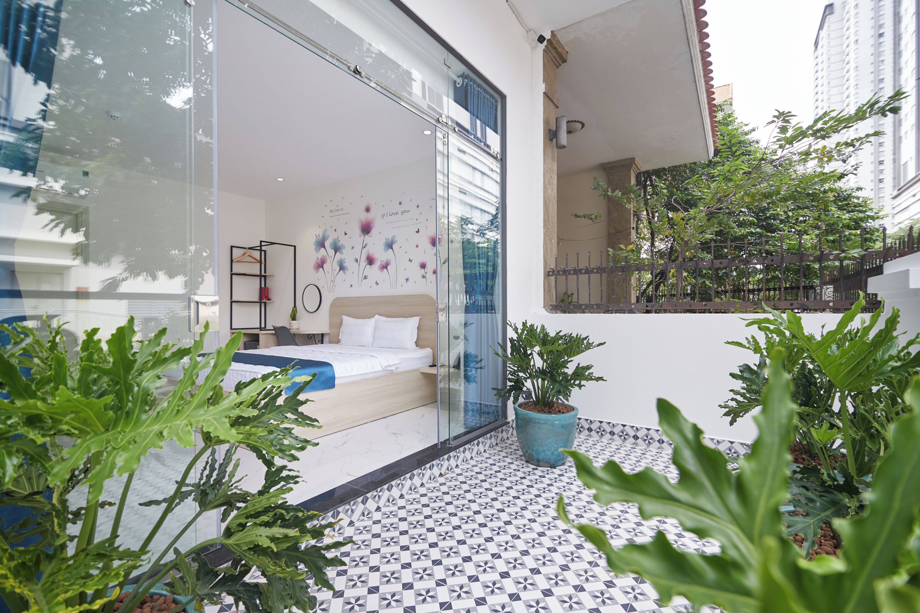 Una habitación de hotel moderna con una cama, una puerta de vidrio que da a un balcón y plantas en macetas.