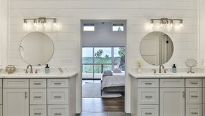 A bathroom with two sinks, a large mirror, and a window leading to a bedroom. - The Cabin On Faraday | Ellijay, GA (Ellijay)