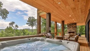 A hot tub on a wooden deck with a stone fireplace and outdoor furniture. - The Cabin On Faraday | Ellijay, GA (Ellijay)