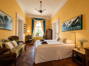 A hotel room with a large bed, a sofa, a desk, and a chandelier.