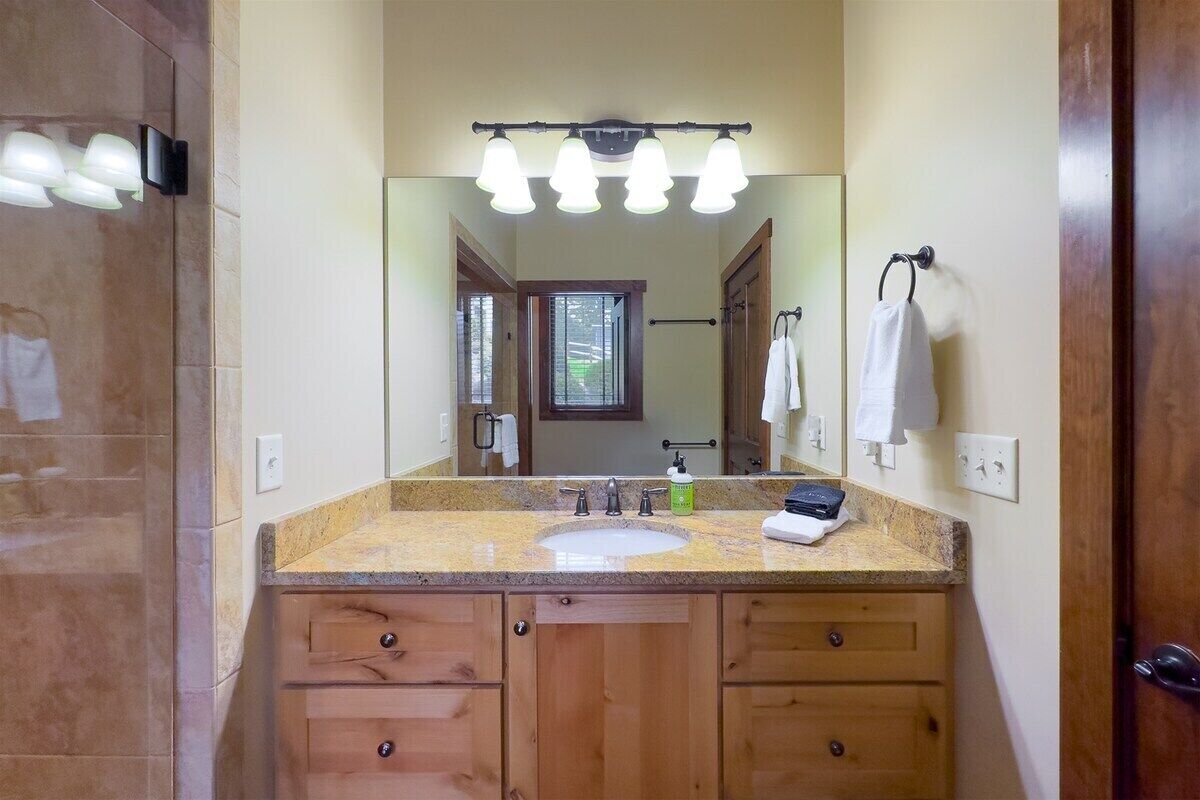 A bathroom with a large mirror, a sink, wooden cabinets, and a vanity light fixture.