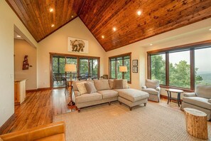A spacious living area with a large sectional sofa, a wooden ceiling, and large windows offering a view of the outdoors. - Oak Cottage in Sutton Knob (Pisgah Forest)