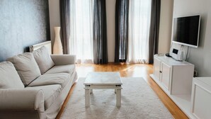 Una sala de estar moderna con un sofá color beige, una mesa de centro blanca y un televisor sobre un mueble blanco.