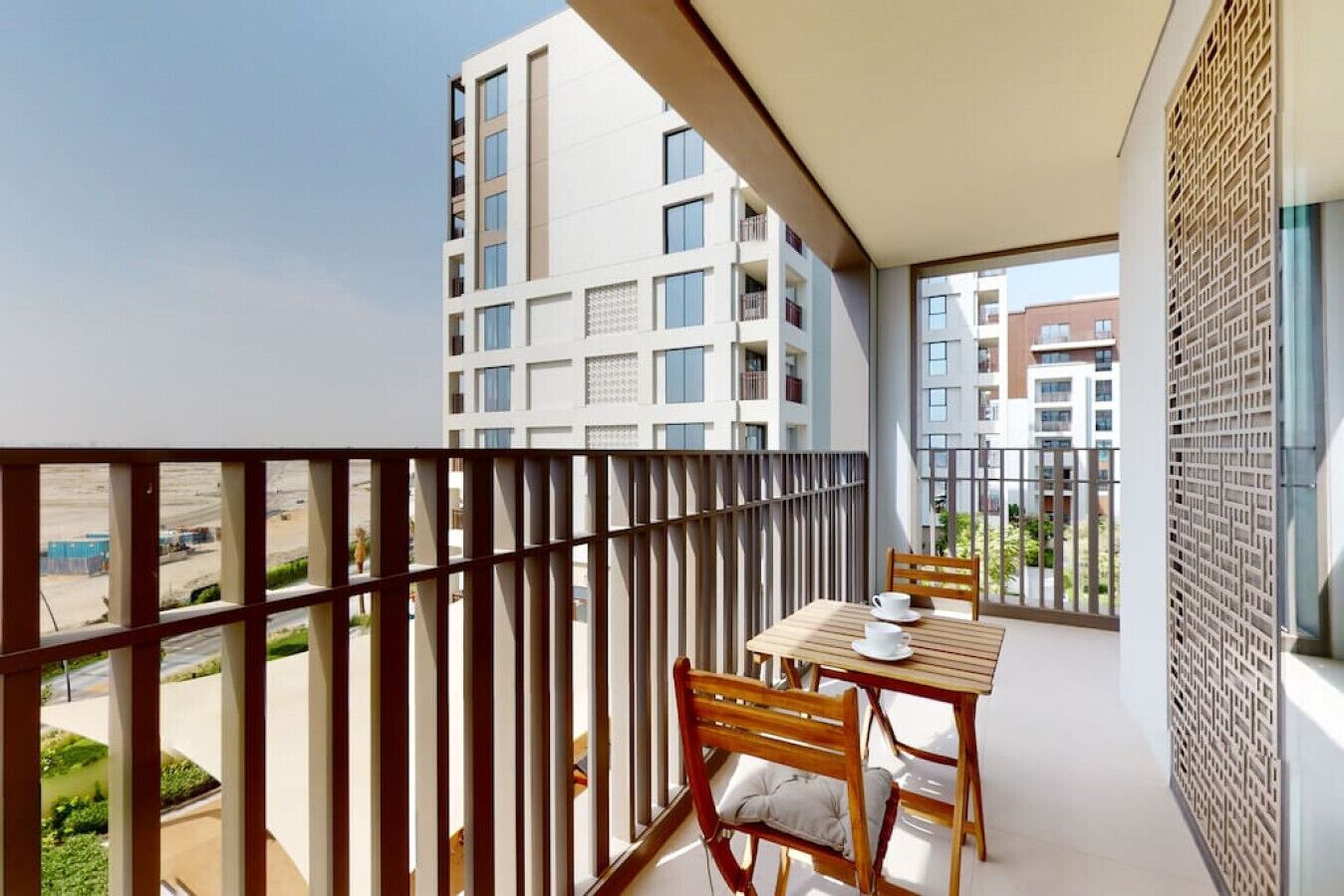 A balcony with a table and chairs, a view of other buildings, and a metal fence.