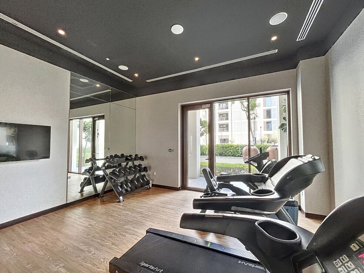 Ein Fitnessraum mit Laufbändern, Kurzhanteln und einer Spiegelwand.