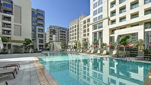 Una piscina con sillones de descanso y sombrillas, rodeada de edificios de varios pisos.