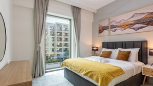 Una habitación de hotel moderna con una cama grande, una mesita de noche, una lámpara y vistas a la ciudad a través de un amplio ventanal.