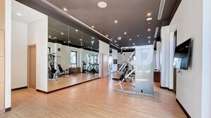 Un gimnasio moderno con equipamiento de ejercicio, un espejo grande y un televisor en la pared.