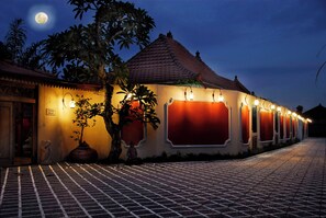 Guests can enjoy a warm and inviting atmosphere at this traditional building, surrounded by lush greenery and beautifully lit windows.