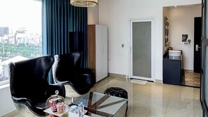 Quarto de hotel moderno com uma grande janela, um candelabro, um sofá, uma mesa de centro e vista para a cidade.