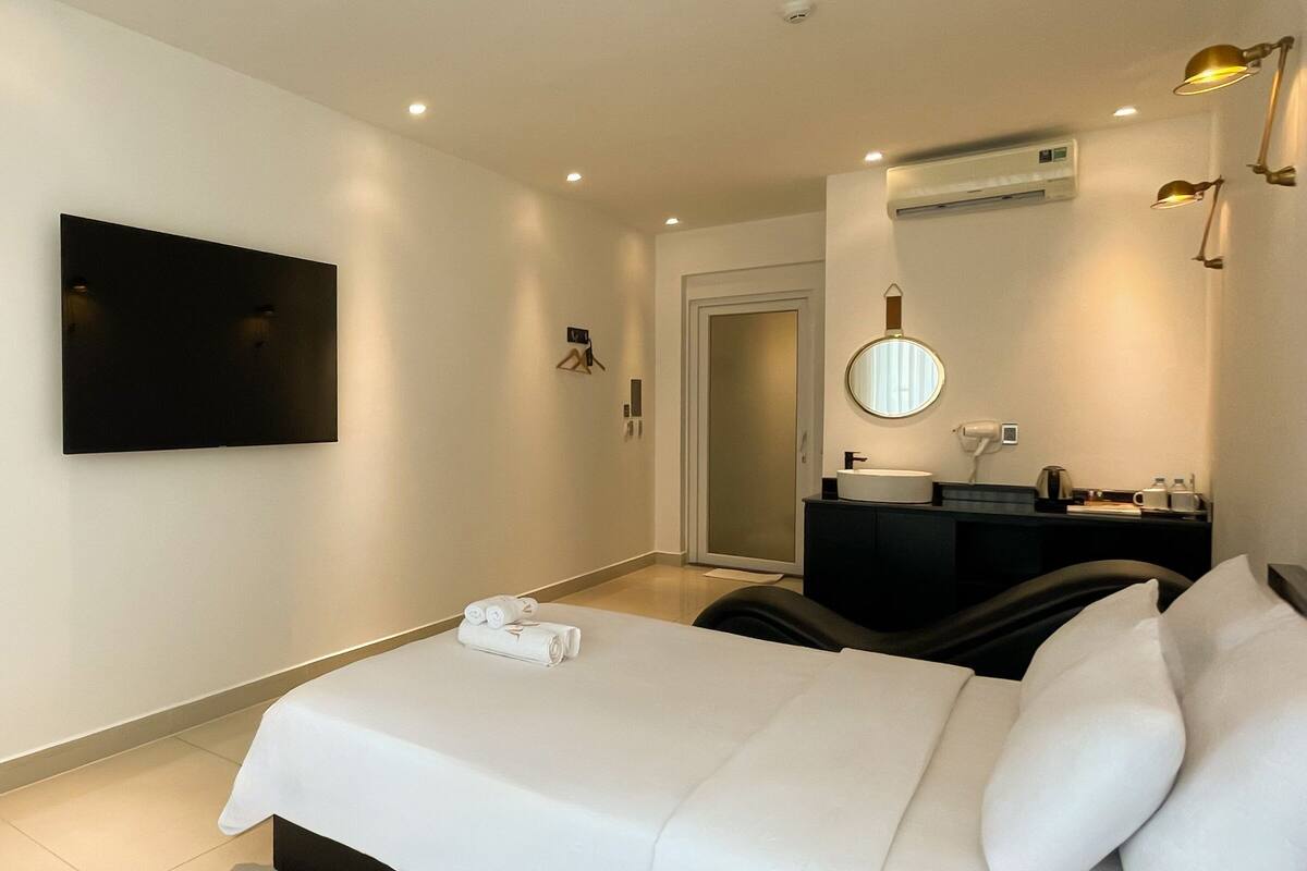 A hotel room with a bed, a TV mounted on the wall, a desk with a mirror, and a small bathroom.