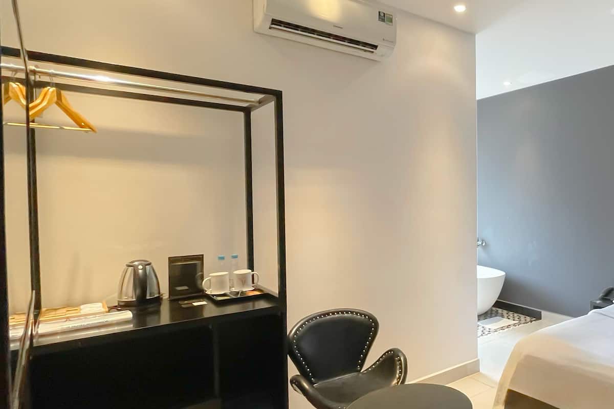 A hotel room with a bed, a desk with a chair, a mirror, and a bathroom with a sink and toilet.