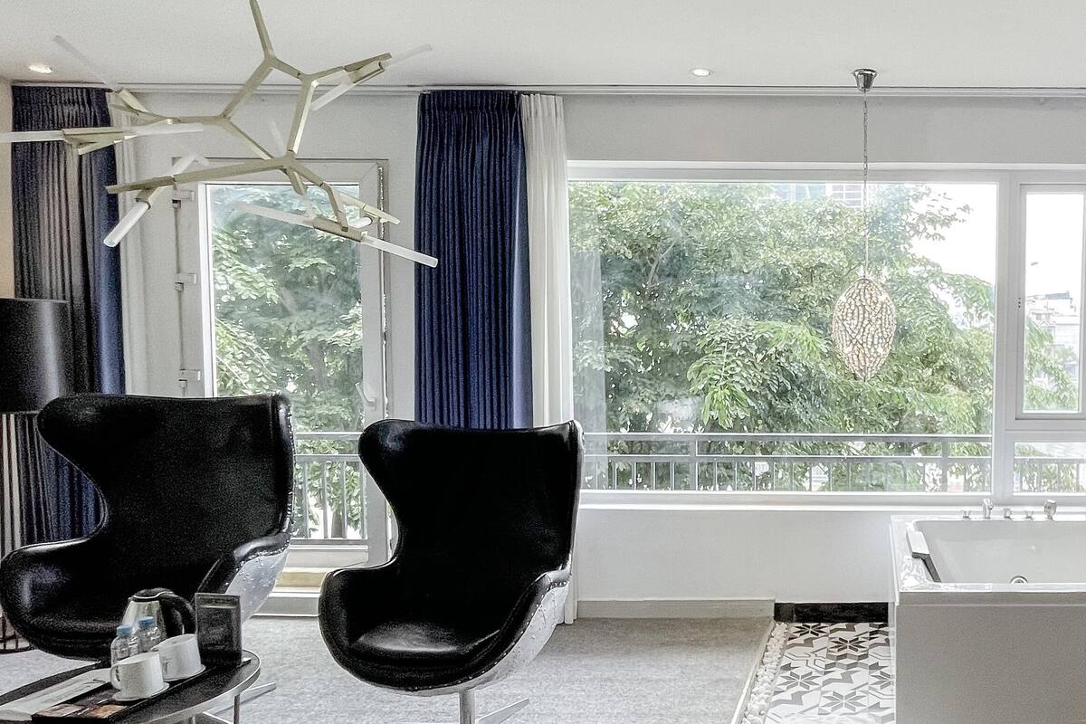 A modern bathroom with a bathtub, a black chair, and a large window with curtains.
