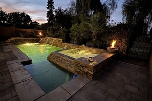 Un área de spa con un jacuzzi y una piscina rectangular, rodeada de muros de piedra y un patio de ladrillo.