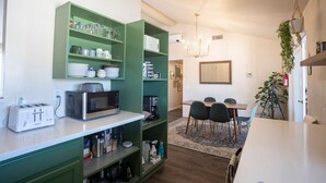 Cocina compacta con armarios verdes, microondas, tostadora y cafetera. Cuenta con un comedor con mesa y sillas.