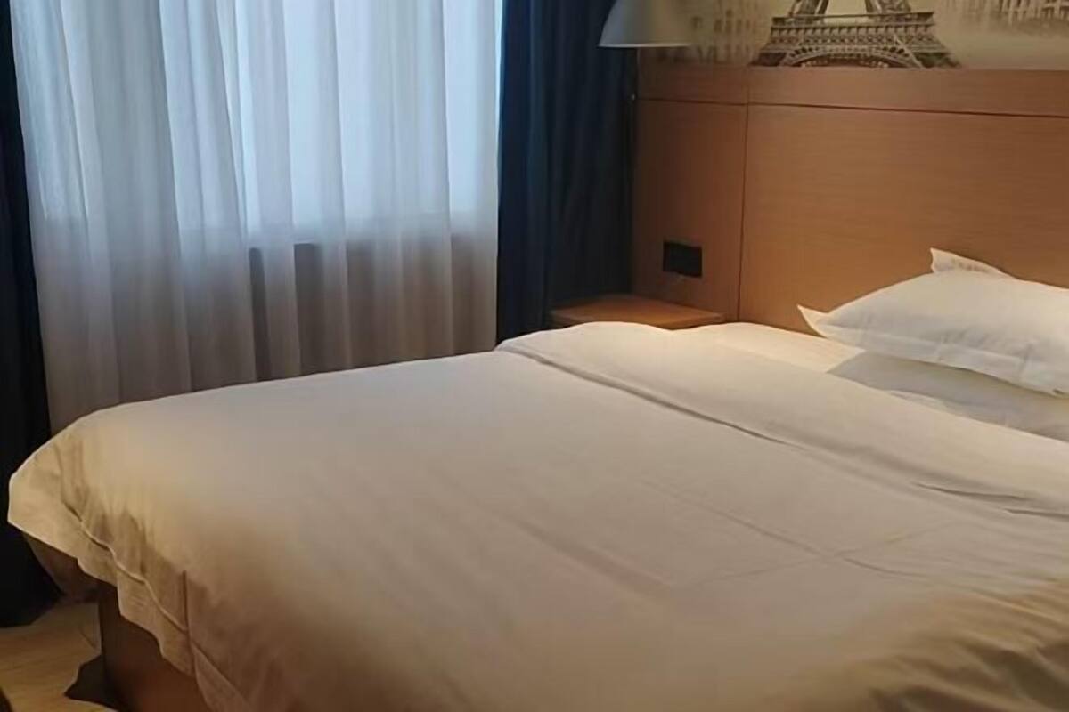 A hotel room with a bed, curtains, a nightstand, and a wall-mounted lamp.