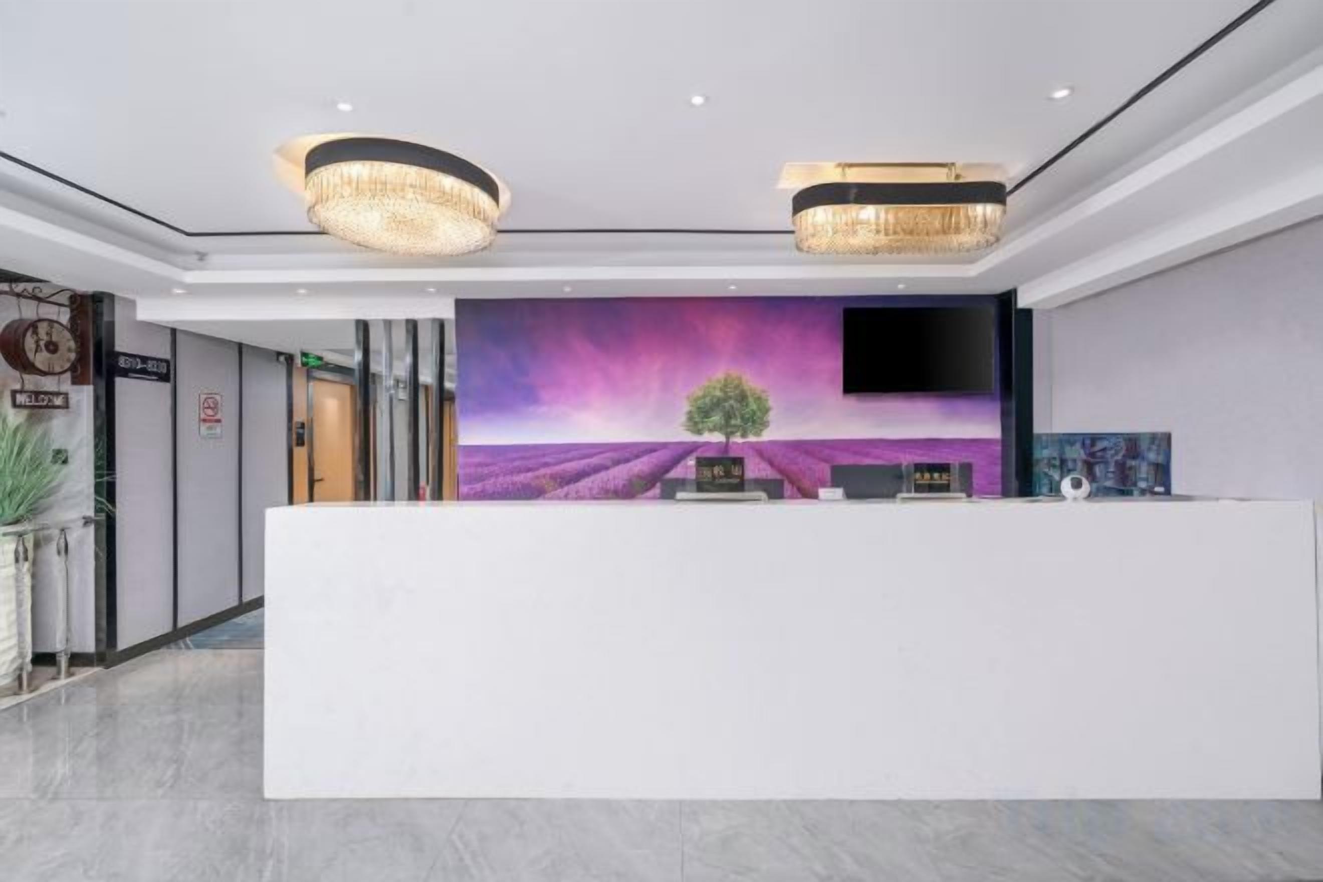 A reception desk with a modern design, a large screen displaying a purple landscape, and a chandelier above.