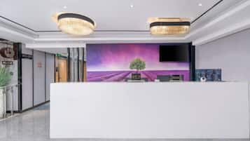 A reception desk with a modern design, a large screen displaying a purple landscape, and a chandelier above.