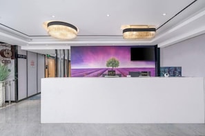 Um balcão de atendimento com design moderno, uma tela grande exibindo uma paisagem roxa e um candelabro acima.