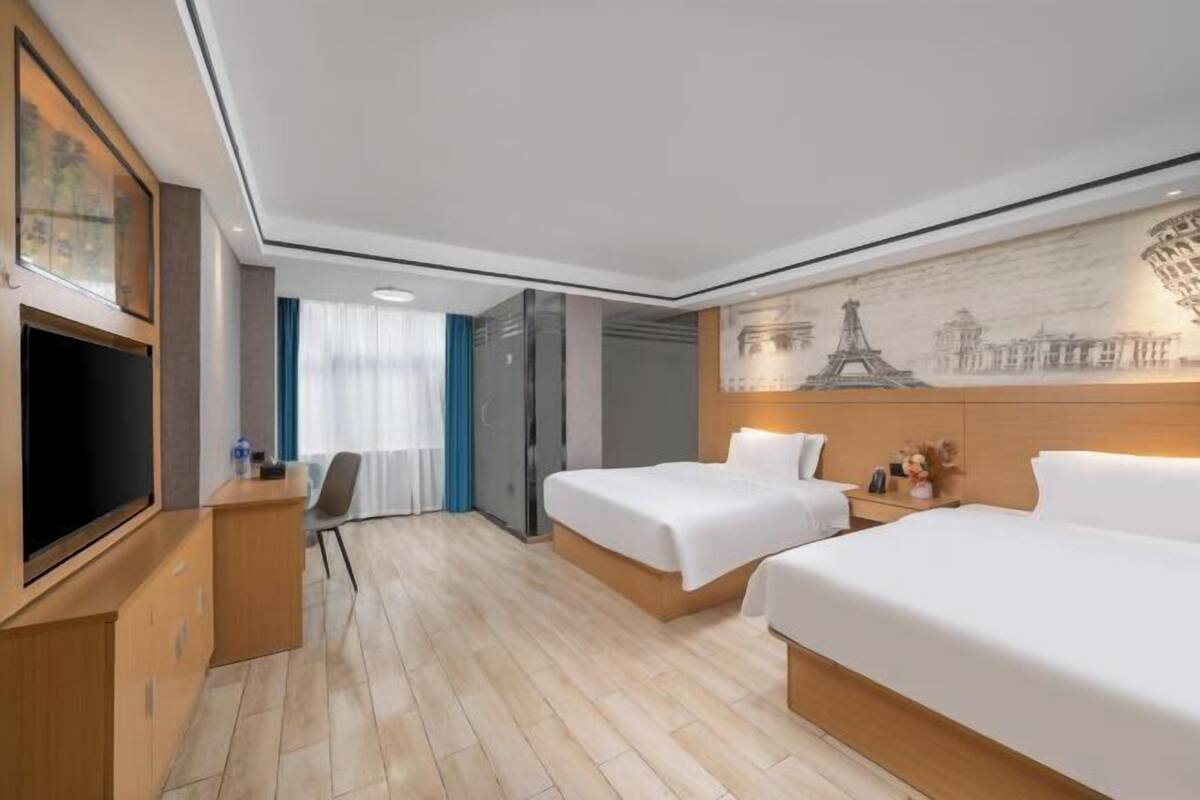 A hotel room with two beds, a desk, a TV, and a mural of Parisian landmarks.