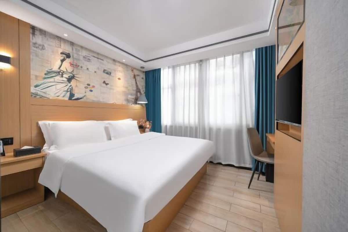 A hotel room with a large bed, a nightstand, a desk with a chair, a TV, and a mural on the wall.