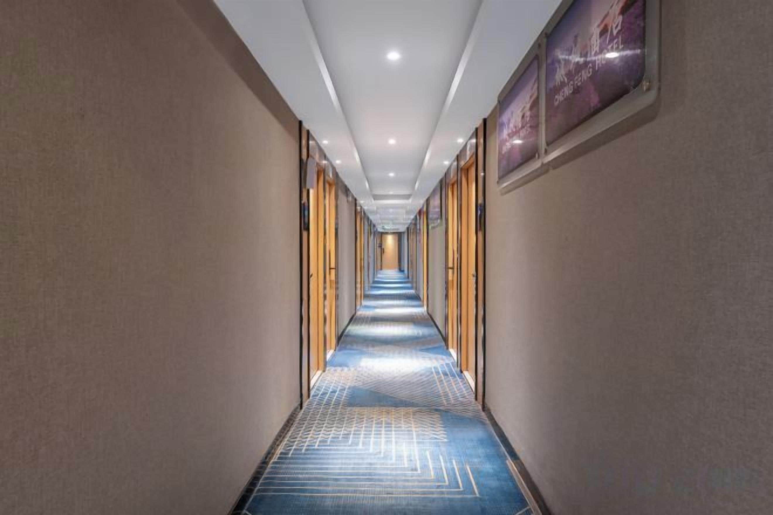 A hotel corridor with a patterned carpet, wooden doors, and framed artwork on the walls.