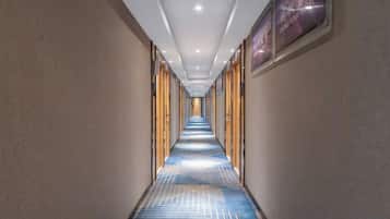 A hotel corridor with a patterned carpet, wooden doors, and framed artwork on the walls.