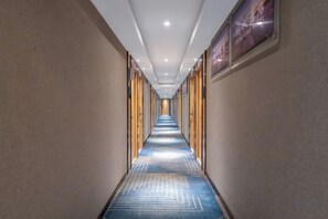 A hotel corridor with a patterned carpet, wooden doors, and framed artwork on the walls. - Yinuo Hotel (Guangzhou Chenjiaci Caihongqiao Metro Station) (Guangzhou)