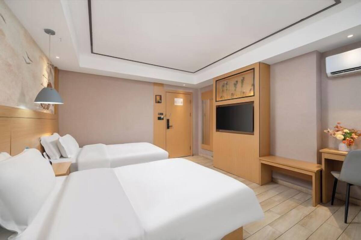 A hotel room with two beds, a desk, a chair, a TV, and a bench.