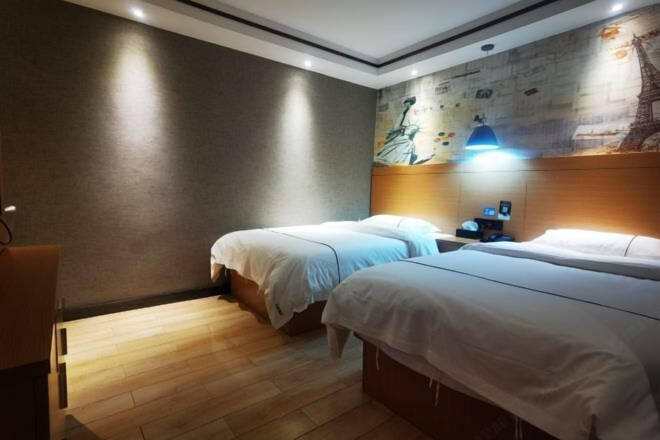 Ett hotellrum med två sängar, ett trägolv, en väggmålning och ett nattduksbord med en lampa.