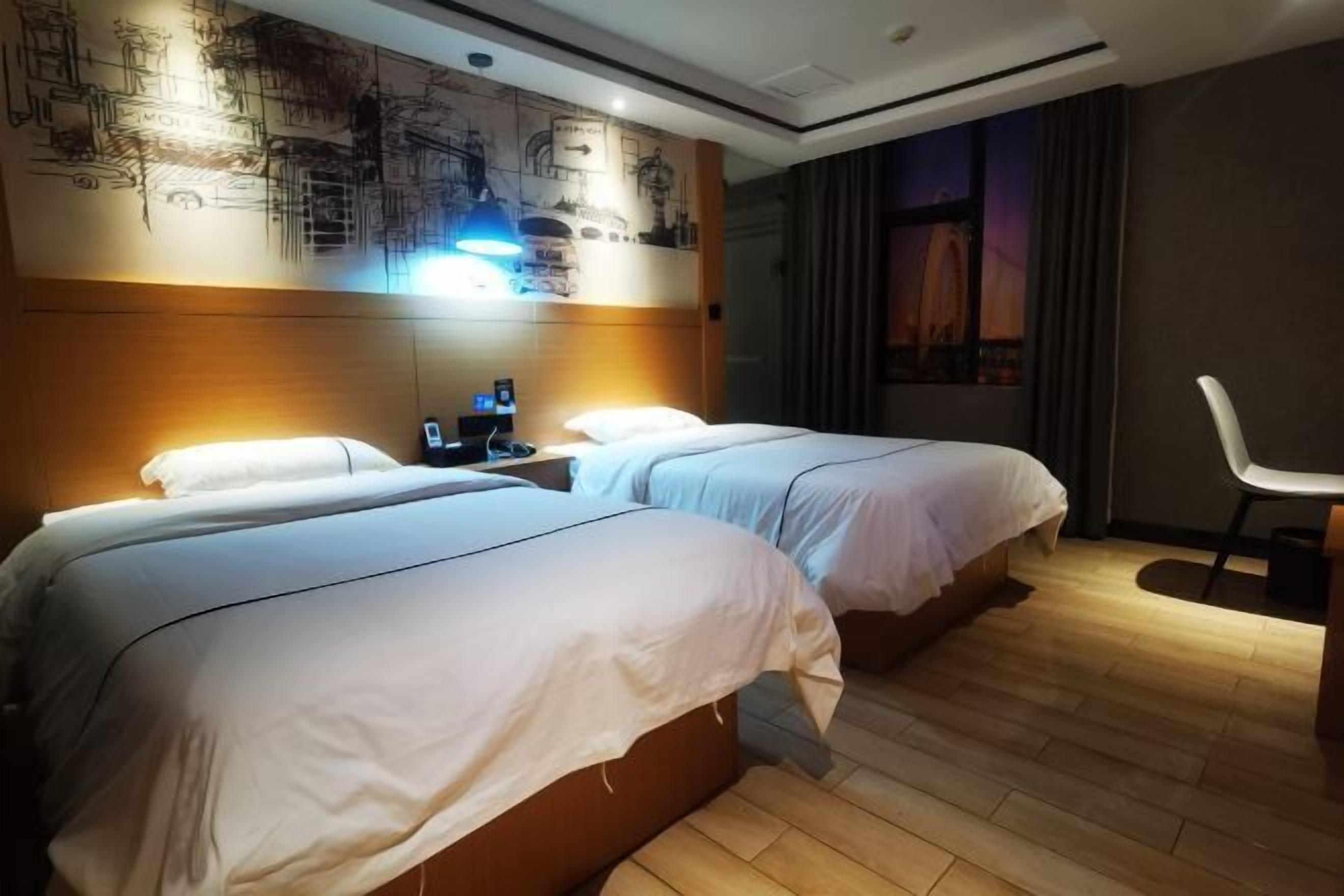 A hotel room with two beds, a nightstand, a desk, and a chair.