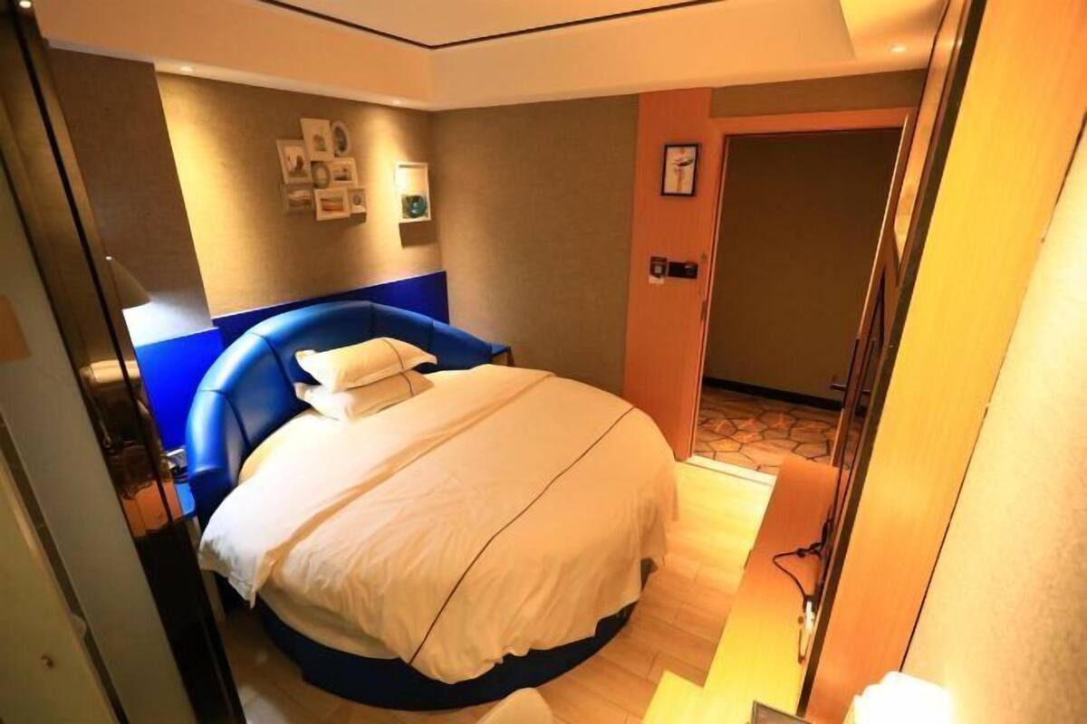 A hotel room with a large bed, a blue headboard, and a small bedside table.