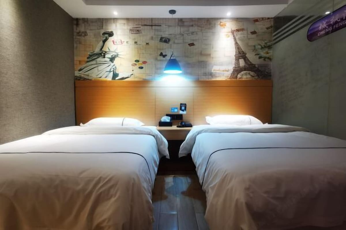 A hotel room with two beds, a wooden headboard, a wall mural, and a nightstand with a lamp.