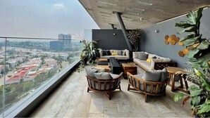 Ein modernes Wohnzimmer mit einer Sofagarnitur, Couchtisch und Sesseln, mit Blick auf eine Stadtlandschaft.