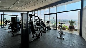 Ein Fitnessstudio mit unterschiedlichen Trainingsgeräten, großen Fenstern und Blick auf die Stadt.
