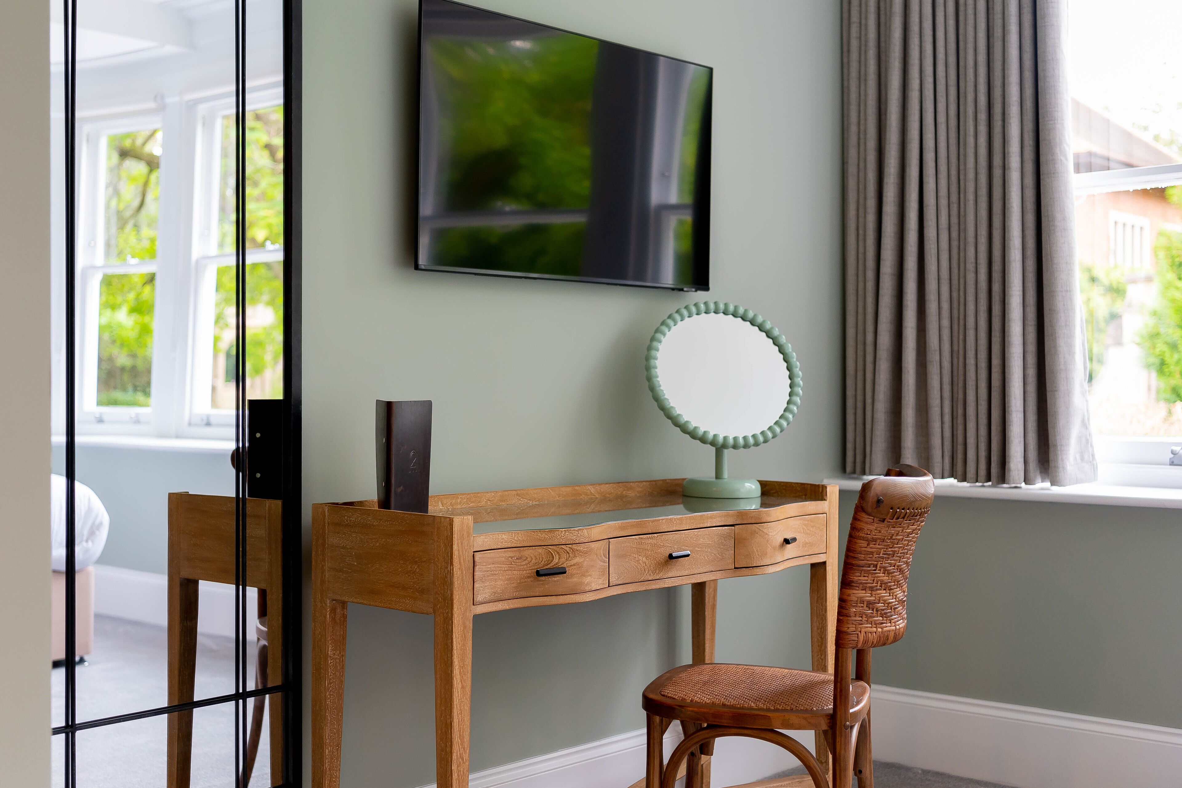 A wooden desk with a mirror and a flat-screen TV mounted on the wall.