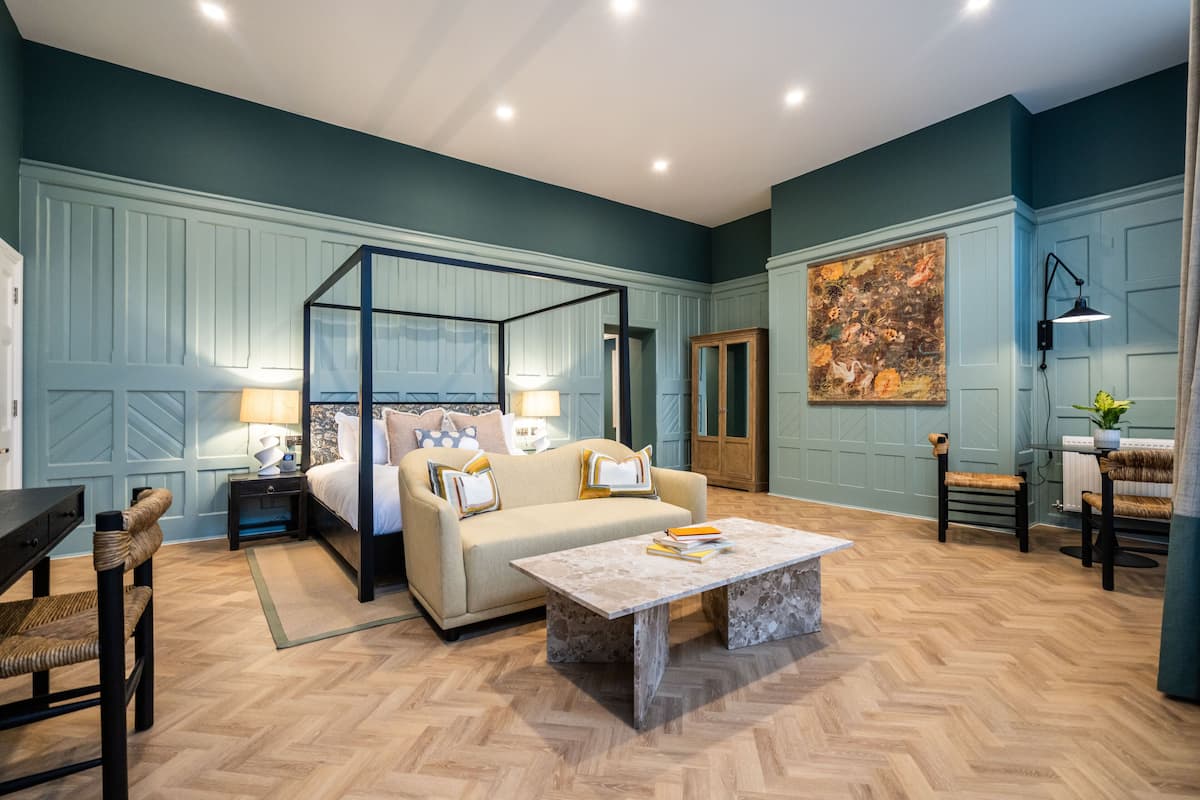 Een kamer met een hemelbed, een bank, een salontafel en een schilderij aan de muur.