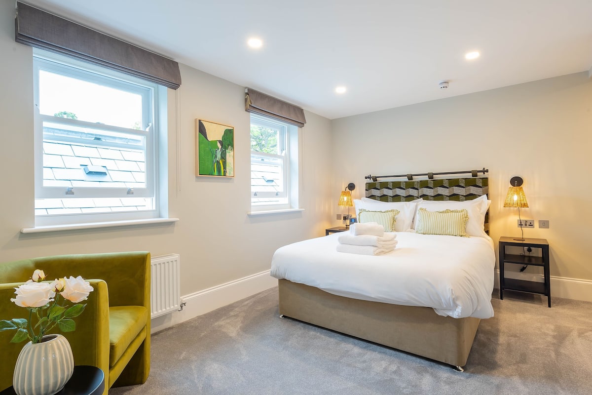 Een slaapkamer met een groot bed, twee bedlampen, een radiator en een raam met gordijnen.