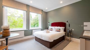 Un dormitorio moderno con una cama grande, una mesita de noche, una lámpara y vistas al verdor exterior.
