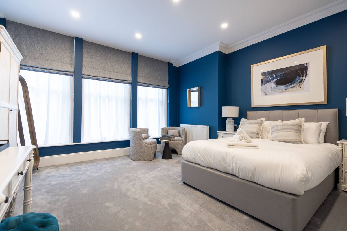 Een slaapkamer met een groot bed, een nachtkastje, een stoel en een raam met gordijnen.