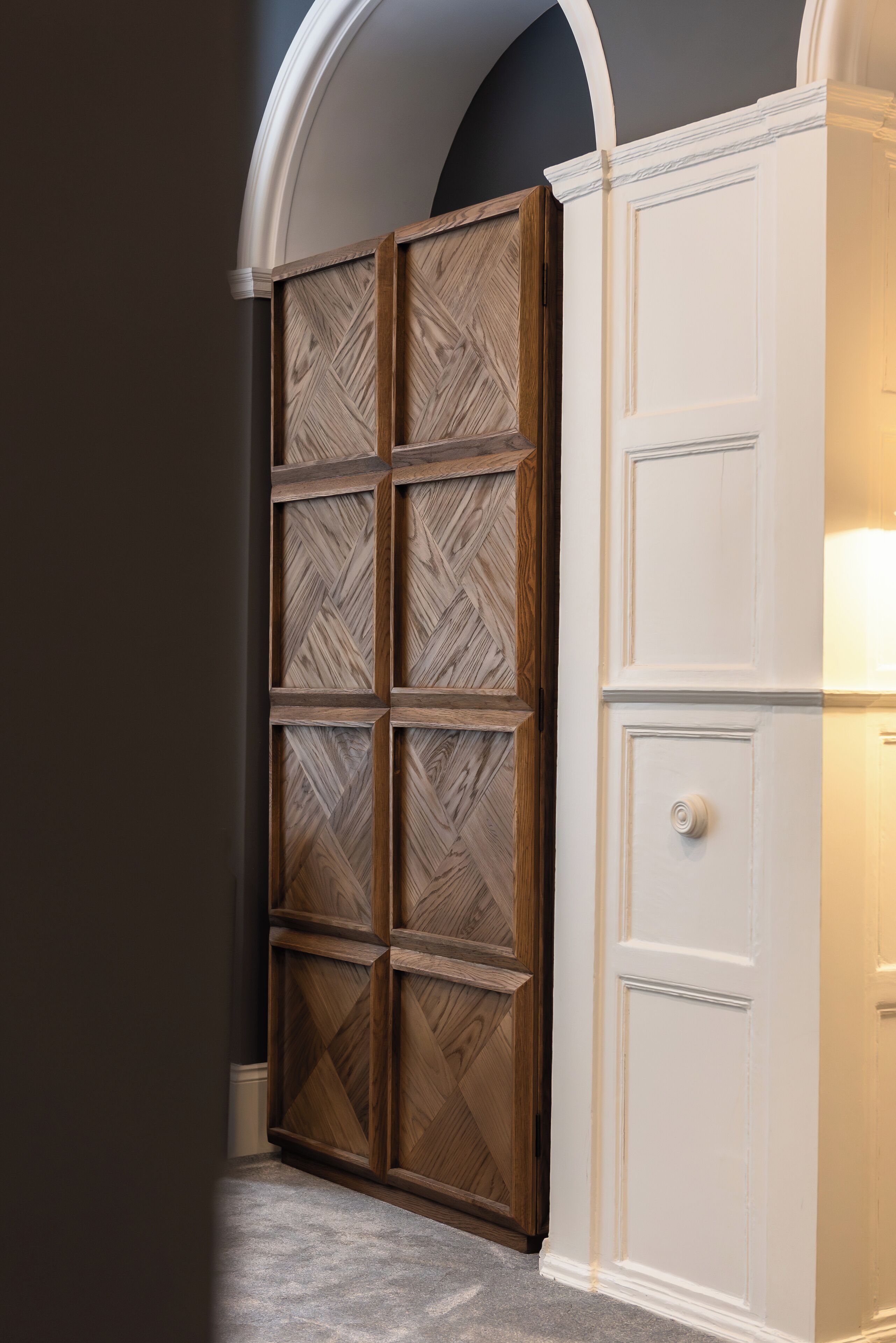 Een kamer met een grote houten garderobe, een wit kastje en een grijs vloerkleed.