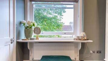 Ett badrum med ett fönster, en radiator, en grön pall och en vas med blommor.