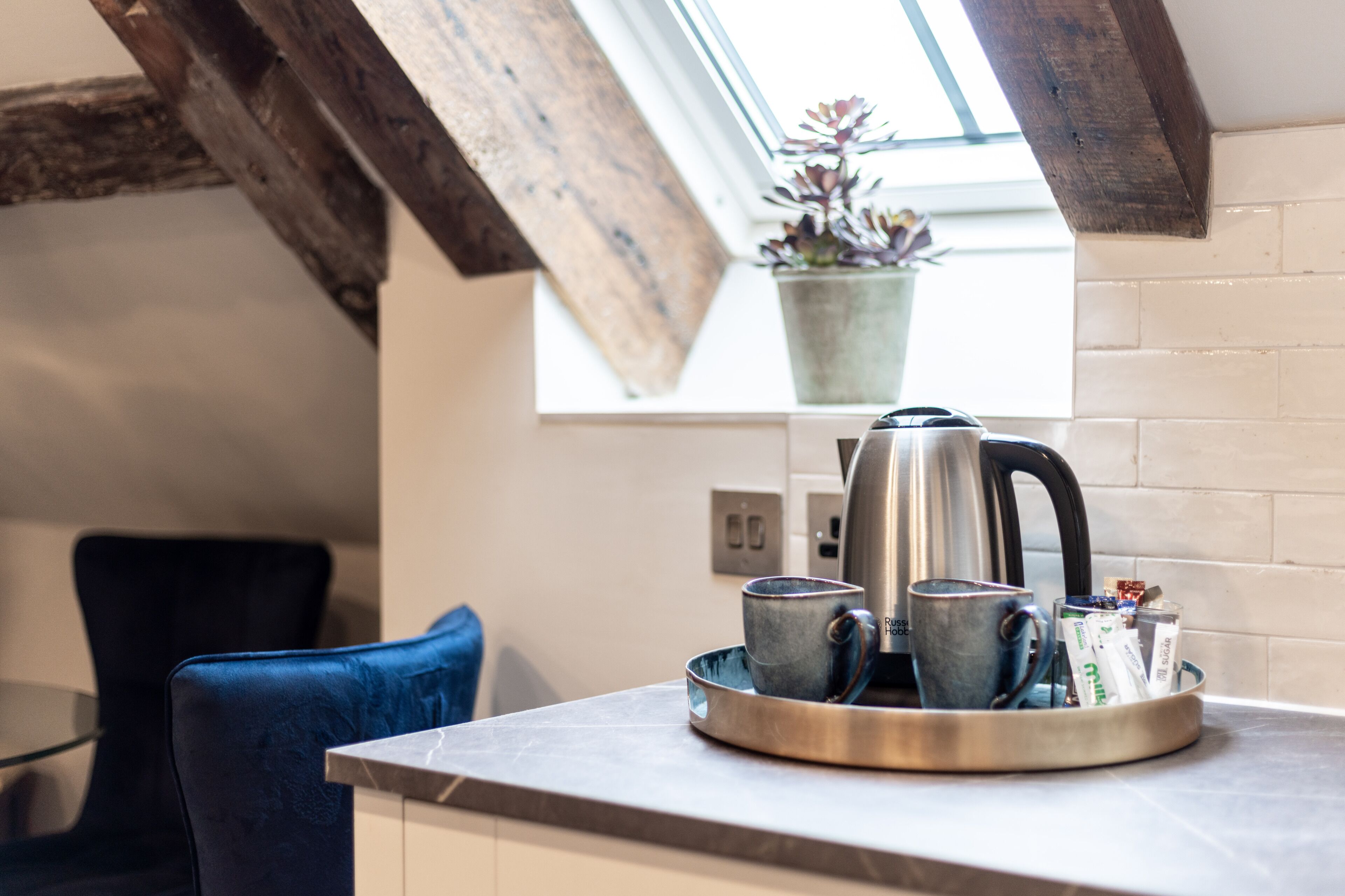 Et køkken med kaffemaskine, kopper og en bakke på bordet.