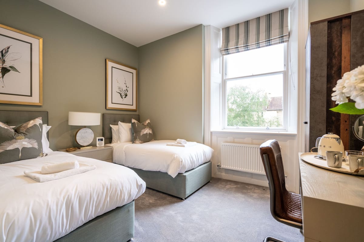 Een hotelkamer met twee bedden, een bureau met stoel, een raam met uitzicht, en kunstwerken in lijsten aan de muur.