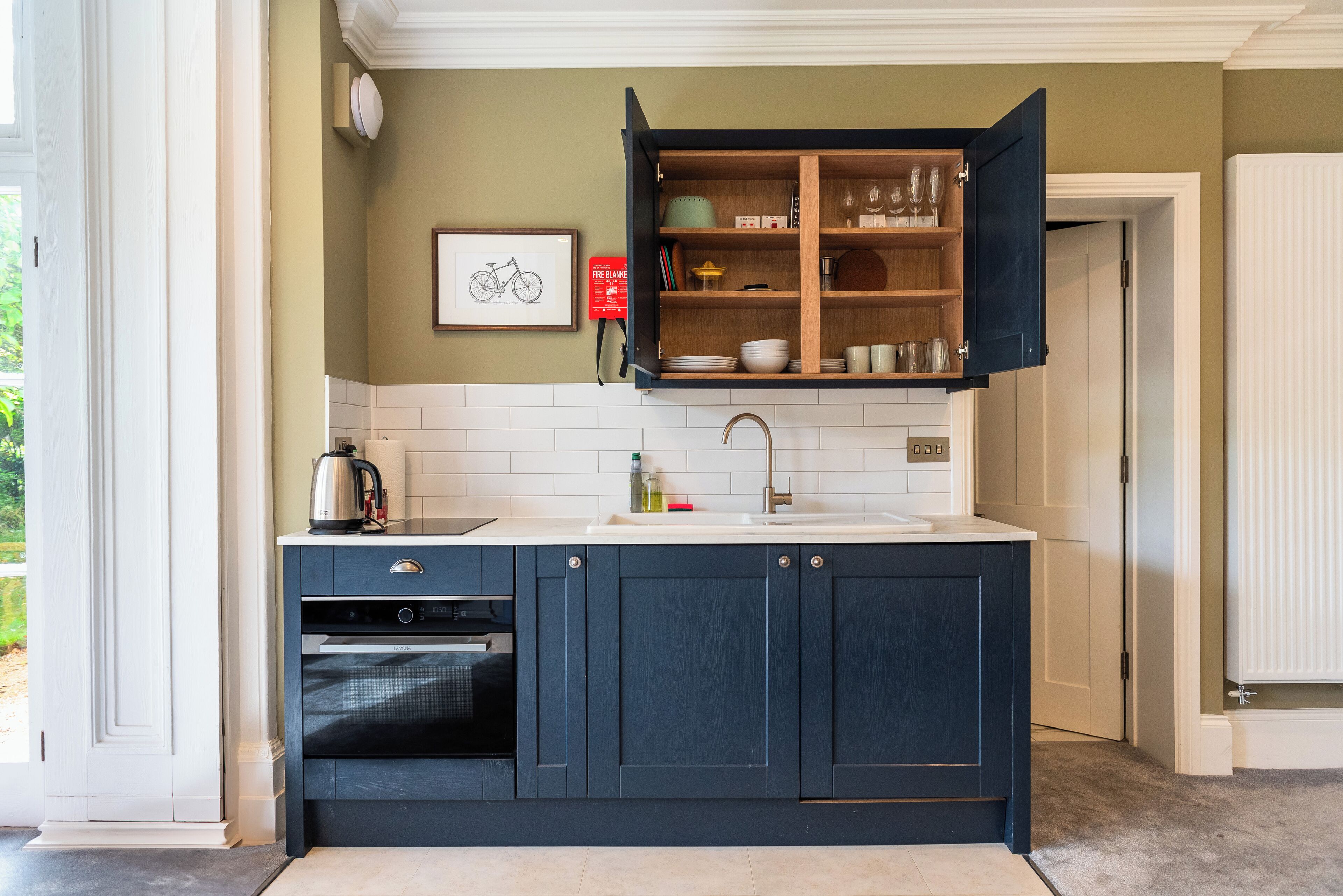 Una cocina con gabinetes azul oscuro, una encimera blanca y un mueble empotrado con cristalería.